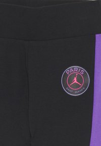 Schwarze Jogginghosen mit einem breiten Bund, ausgestattet mit einem lila Akzent und einem runden Logo mit "PARIS SAINT-GERMAIN" in Pink und Schwarz.