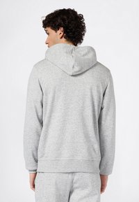 Sudadera con capucha de color gris claro hecha de tela suave y texturizada. Cuenta con un bolsillo tipo canguro, puños acanalados y un diseño de ajuste relajado.
