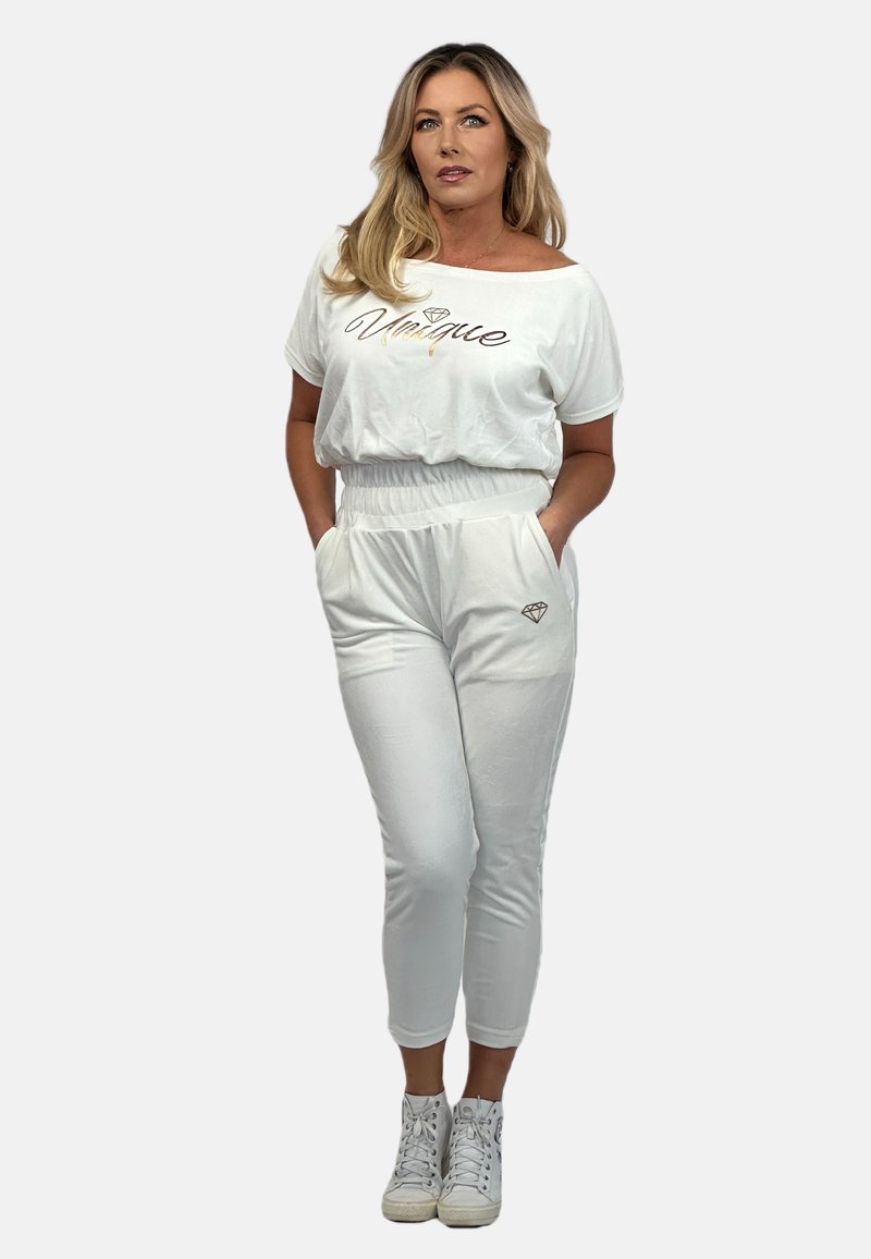 Biały bawełniany zestaw składający się z luźnej koszuli i zwężanych spodni, ozdobiony napisem "Unique" oraz ikoną diamentu na kieszeni. Stylizowany z białymi sneakersami.