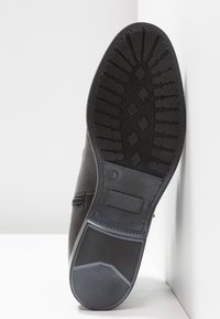 Černá kožená bota s texturovanou gumovou podrážkou, která má pro grip cikcakový vzor a vyražené logo na patě.