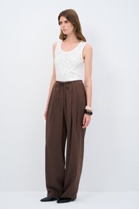 Witte mouwloze top met strass versieringen, gecombineerd met hooggerokte, vloeiende bruine broeken en zwarte puntige schoenen.