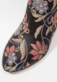 Bottine noire en tissu avec des motifs floraux roses et bleus, à bout pointu et surface texturée. Couture décorative accentuée visible.
