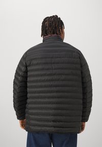 Sort pufferjakke med horisontalt quiltet design, høj krave og elastiske manchetter. Materialet ser let og vandafvisende ud.