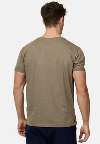 Olivengrünes T-Shirt mit kurzen, aufgerollten Ärmeln und einem Rundhalsausschnitt. Der Stoff wirkt weich mit einer subtilen Textur. Keine sichtbaren Grafiken oder Muster.