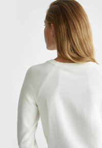Felpa bianca con collo rotondo a coste, maniche raglan con cuciture sottili e una morbida texture in maglia.