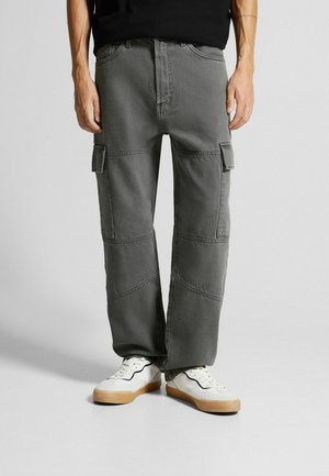 Pantalones cargo grises de algodón con un ajuste relajado, que cuentan con múltiples bolsillos laterales y detalles de costura en contraste. Combinados con zapatillas blancas.