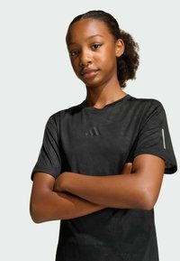Black athletic t-shirt with a textured pattern, featuring a small logo on the chest and reflective accents on the sleeves. Short-sleeved design.