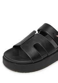 Black slide sandal featuring a smooth leather upper with three wide straps, a contoured footbed, and a thick rubber sole.