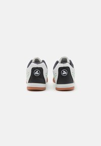 Zapatillas deportivas blancas con acentos en negro, parte superior de malla texturizada y suela de goma; detalles en verde en los laterales; logo en el talón.