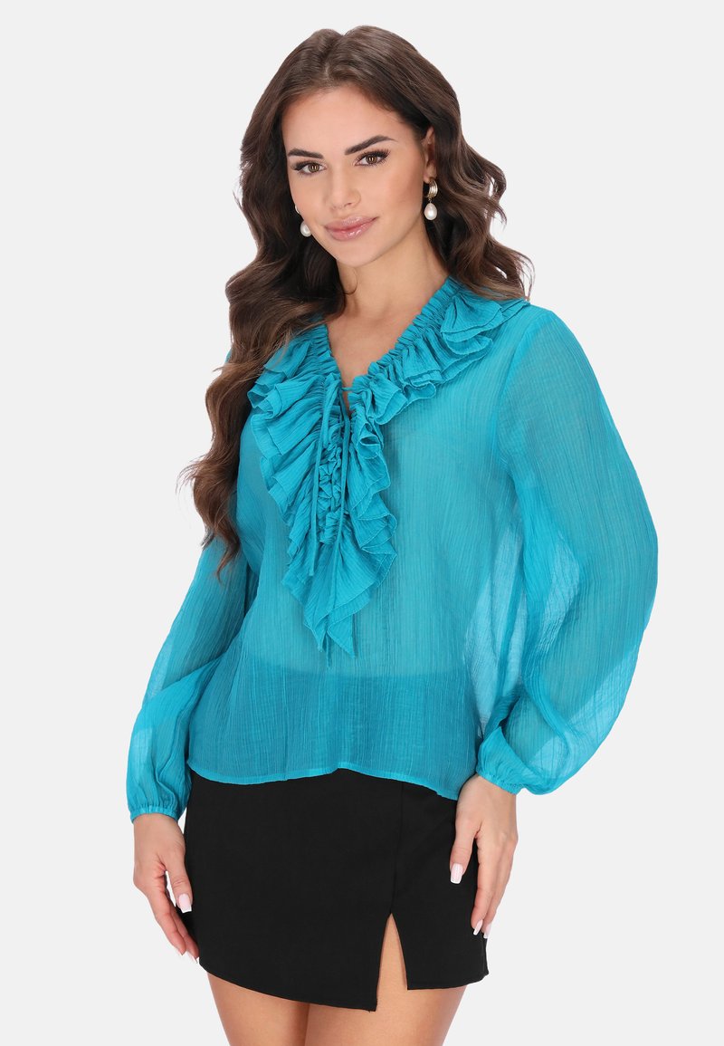 Turkusowa bluzka z falbaniastym dekoltem i mankietami, wykonana z przezroczystego materiału. Połączona z czarną spódnico-shortsami z bocznym rozcięciem.