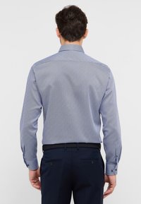 Camicia aderente a maniche lunghe di colore blu navy con un motivo geometrico bianco. Presenta un colletto classico e polsini con bottoni, realizzata in un tessuto liscio.