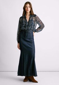 Sheer blouse dengan pola bunga dan lengan panjang, dipadukan dengan rok maxi denim gelap berpinggang tinggi yang memiliki belahan depan dan jahitan detail.