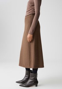 Gonna midi in lana marrone con taglio dritto, abbinata a leggings neri e stivaletti in pelle con punta a stiletto, vista laterale.