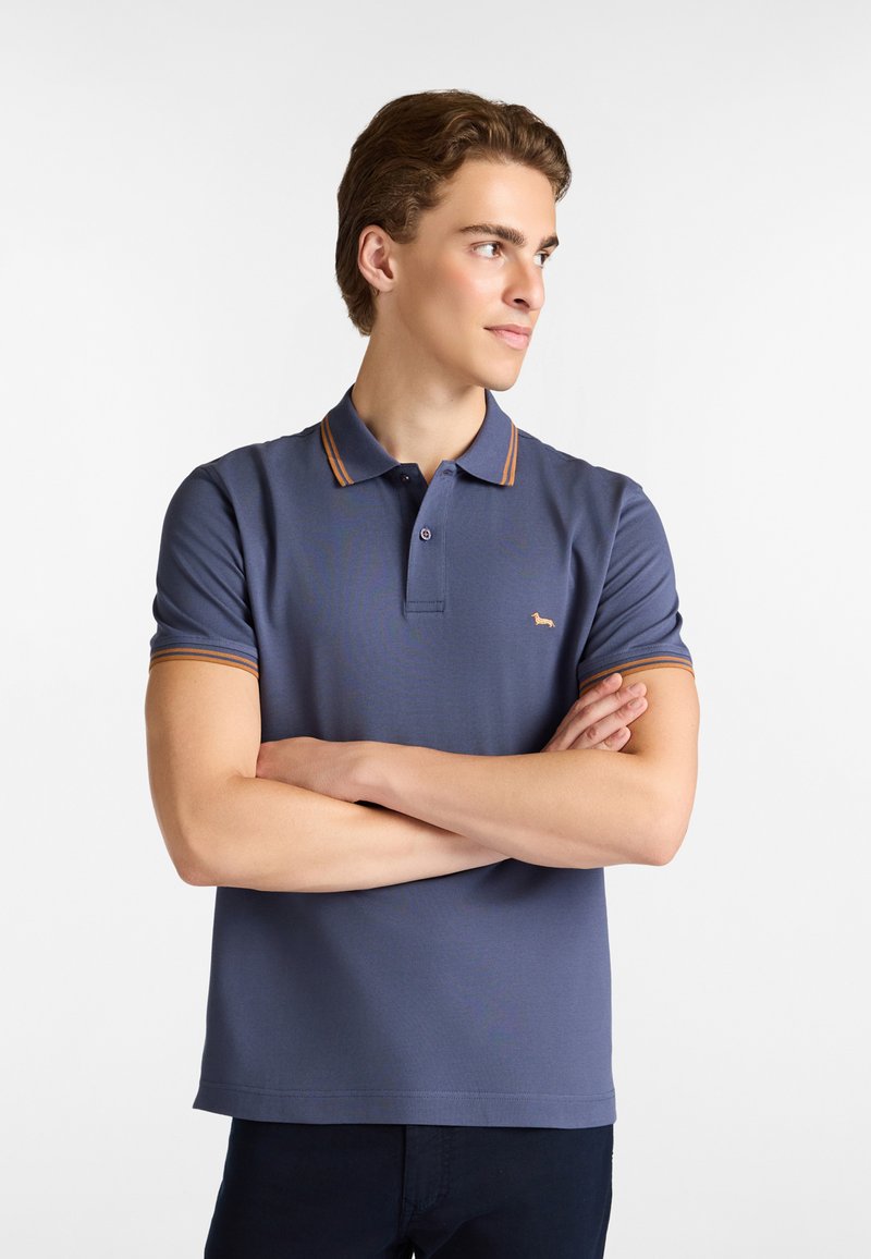 Polo tričko s krátkym rukávom, námorníckej modrej farby s golierom s oranžovými pruhmi, ktorý obsahuje malé vyšívané logo na hrudi a má klasický strih.