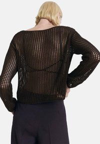Brązowy sweter dzianinowy o otwartej siatkowej konstrukcji, z długimi rękawami i luźnym krojem, eksponujący teksturowany wzór na plecach.