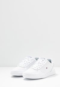 Weiße Sneaker mit einem glatten synthetischen Obermaterial, Schnürverschluss, drei seitlichen Streifen und einem markierten Zungenlabel. Strukturiertes Gummisohle.