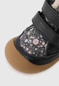 Melna mākslīgās ādas kurpe ar ziedu rakstu audumu uz augšdaļas, aprīkota ar divām spiedpogu siksnām un teksturētu gumijas zoli.