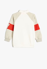 Sudadera blanca con mangas grises que presenta una franja roja y detalles numéricos. Confeccionada en material suave, con un alto cuello y puños de canalé.