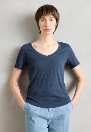 Navy blue short-sleeve t-shirt with a v-neck design, made of soft, textured fabric. Paired with light blue jeans, hands in pockets.
