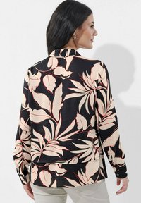 Schwarzes Langarmshirt mit einem floralen Muster in Creme und Rot. Mit Kragen und Knopfmanschetten, aus einem leichten Stoff gefertigt.