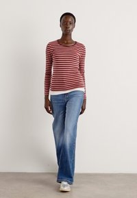 Camicia a maniche lunghe a righe rosse e bianche abbinata a jeans a gamba larga blu chiaro, indossata con scarpe bianche. Texture liscia, vestibilità casual.
