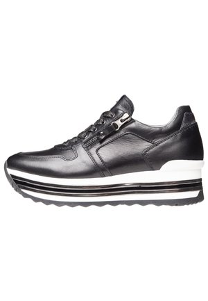 Baskets en cuir noir avec une semelle épaisse rayée blanche et noire, des lacets et une fermeture éclair latérale sur fond blanc uni.