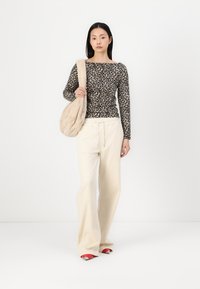 Top din bumbac cu imprimeu leopard și mâneci lungi, pantaloni largi crem și pantofi roșii slip-on. Poartă o geantă de umăr din blană ecologică bej. Fundal curat.