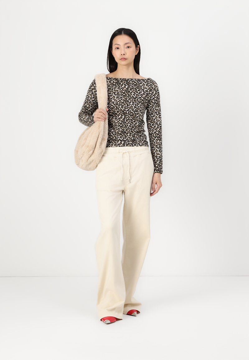 Haut à manches longues imprimé léopard, pantalon large crème et chaussures rouges à enfiler. Portant un sac à épaule en fausse fourrure beige. Fond propre.