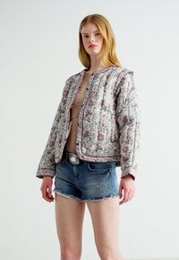 Jachetă cu umplutură florală, cu un model roz și alb, având un guler rotund, mâneci lungi și o croială ajustată, asortată cu pantaloni scurți din denim.