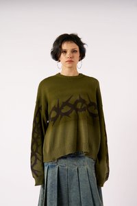 Ελιά πράσινος πλεκτός σκούφος με σκούρο καφέ αφηρημένο σχέδιο, ραβδωτός λαιμός και μακριά μανίκια, συνδυασμένος με πλισέ τζιν φούστα.