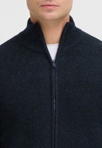 Donkerblauwe ritsbreisweater met een gestructureerd breipatroon, hoge kraag en metalen rits. Lichtgewicht en geschikt voor lagen.