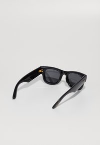 Black plastic sunglasses with gray lenses, square-shaped frames, and gold accents on the temples, featuring a smooth texture.