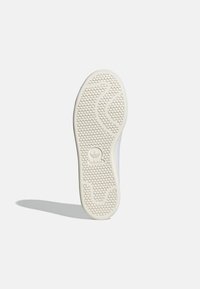 Bílá podrážka tenisky s texturovaným šestihranným vzorem, s centrálním logem značky. Hladký, zaoblený tvar s minimem designových detailů.