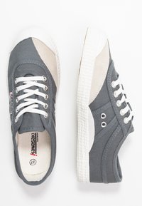 Sneaker in tela grigia con suole in gomma bianca, dotate di dettagli beige, occhielli metallici rotondi e lacci bianchi. Texture liscia in tutto il modello.