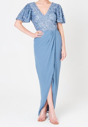 Femme portant un haut bleu à sequins avec manches bouffantes et une jupe drapée assortie avec une fente à l'avant, associée à des talons à brides transparentes.