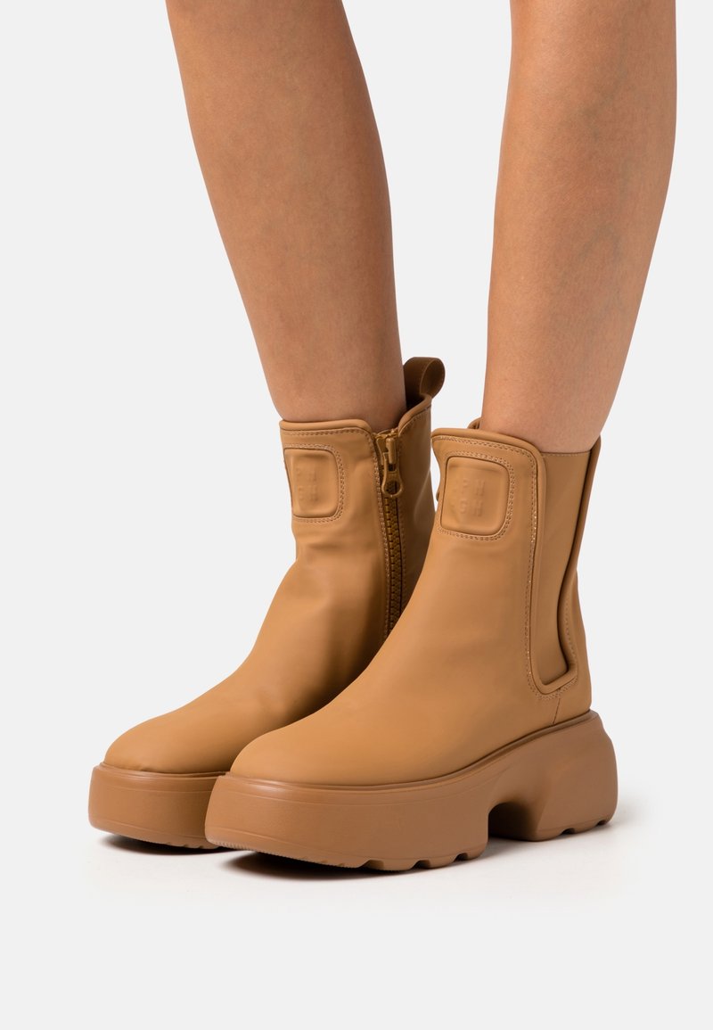 Hellbraune Knöchelstiefel aus glattem Leder mit seitlichem Reißverschluss, elastischen Einsätzen und einer klobigen Plateausohle. Schlichtes Design ohne sichtbare Muster.