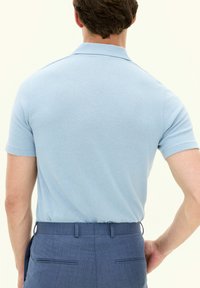 Polo bleu clair à manches courtes, caractérisé par une texture douce. Assorti à un pantalon noir sur mesure, affichant une coupe soignée.