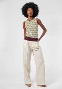 Top senza maniche lavorato a maglia giallo con accenti viola scuro, caratterizzato da un motivo a rombi; abbinato a pantaloni beige a vita alta.