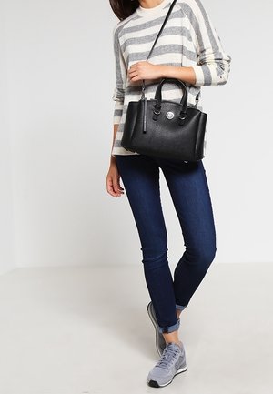 Nainen harmaassa raidallisessa villapaidassa, tummat kapeat farkut, harmaat lenkkarit, pitää mustaa nahkaista olkalaukkua.