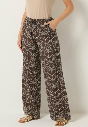 Brune bukser med vide ben med hvid botanisk print, elastisk linning, sidelommer, båret med beige top og guld sandaler.