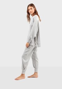 Grijze sweatshirt met ballonmouwen, geribbelde manchetten en een ritssluiting aan de achterkant. Complementaire grijze tapered broek met elastische manchetten en subtiele stiksels.