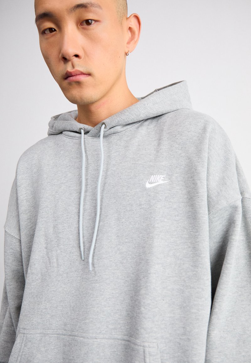 Szara bluza Nike wykonana z miękkiego materiału, z przednią kieszenią, sznurkami do regulacji oraz małym białym logo w górnym lewym rogu klatki piersiowej.