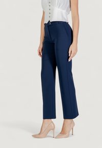 Pantaloni tailored blu navy caratterizzati da un design elegante, tessuto morbido, vita media e piega frontale, abbinati a scarpe con tacco nudo.