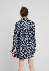 Mörkblå klänning med blommönster i ljusblått, med långa ärmar, ett bälte vid midjan och snören vid ärmsluten.