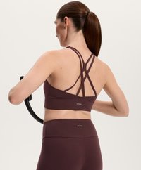 Burgundy sportbh med korsade remmar på ryggen, tillsammans med matchande högmidjade leggings. Slät tyg med subtil logotypdetalj.
