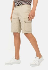 Beige cargoshorts met zijzakken, een vlakke voorkant en een relaxed fit, gecombineerd met witte sneakers met een gestructureerde grijze accenten.