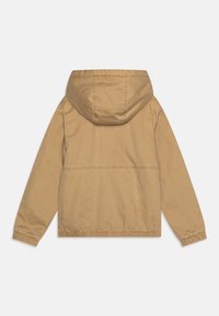 Giacca beige con cappuccio, con polsini e orlo elasticizzati, realizzata in tessuto morbido. Presenta un design semplice senza hardware o motivi visibili.