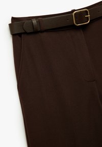 Pantalones marrones de una tela suave, con un corte entallado, bolsillos laterales y un cinturón de cuero marrón a juego con una hebilla dorada.