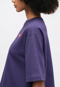 T-shirt in cotone viola con una vestibilità rilassata, maniche corte e un dettaglio del logo rosso sul petto, caratterizzato da un design a girocollo.