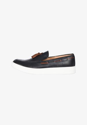 Mocassino slip-on in pelle nera con nappe e dettagli marroni, dotato di suola in gomma bianca.